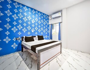 Een slaapkamer met een bed, een blauwe wand met patroon, een airconditioning en een raam met gordijnen.