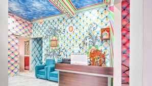 Quarto com teto estampado, sofá azul, balcão de recepção em madeira e parede decorativa.
