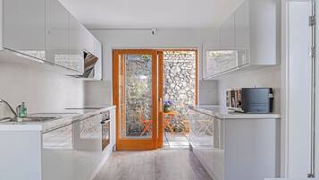 A modern kitchen with a central island, a built-in oven, and a stone wall visible through a glass door.