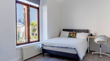 A bedroom with a bed, a window, a radiator, and a desk with a chair.