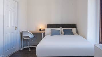 A bedroom with a bed, a chair, a bedside table with a lamp, and a door.