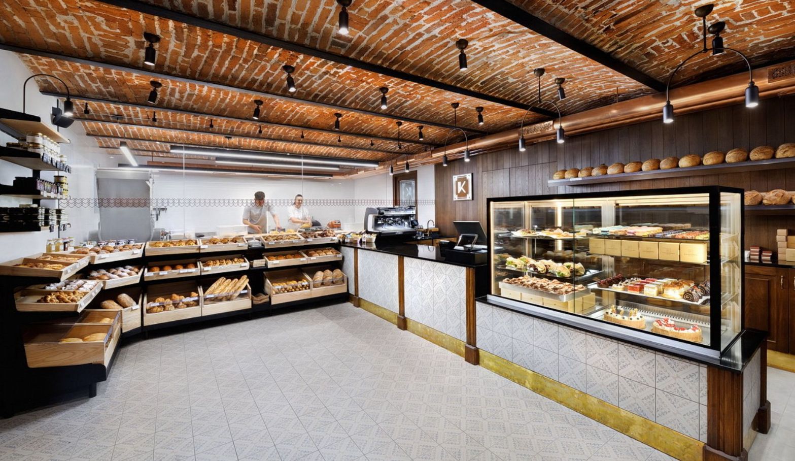 Une boulangerie avec un plafond en briques, des comptoirs en bois et une vitrine remplie de pâtisseries.