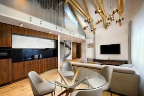 A modern interior with a kitchen, dining area, and living space, featuring a spiral staircase, a flat-screen TV, and a glass table. - Apartmány Kuszmannov bazár (Vysoké Tatry)