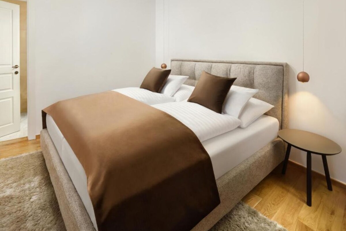 Ein ordentlich bezogenes Bett mit brauner Decke, einem Kopfteil und einem kleinen Nachttisch mit einer Lampe.