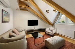 Ein modernes Schlafzimmer im Loft-Stil mit schrägverdeckter Decke, einem großen Fenster, einem Flachbildfernseher, einem Sofa, einem Couchtisch und einem gesteppten Ottoman.
