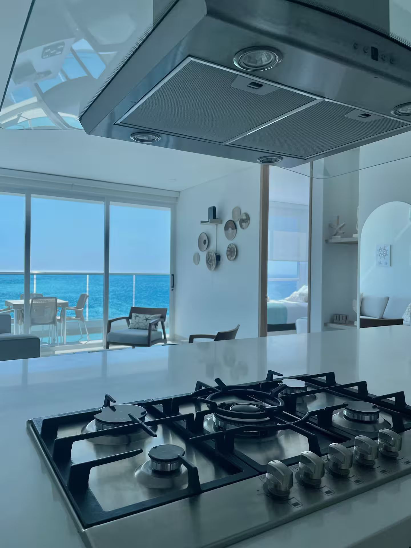A modern kitchen with a gas stove, large windows, and a view of the sea.