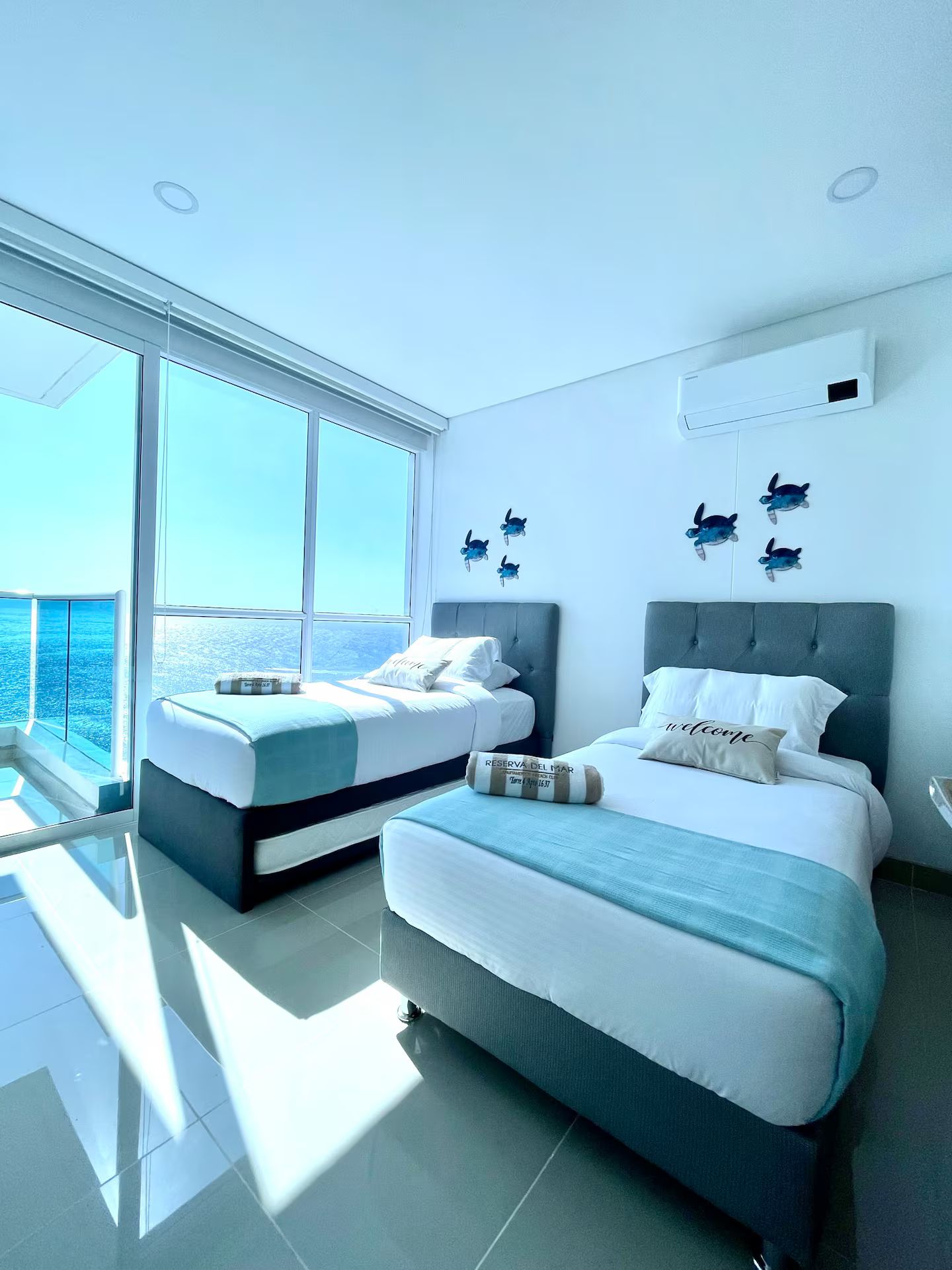 A modern hotel room with two beds, a large window with a view, and a balcony.