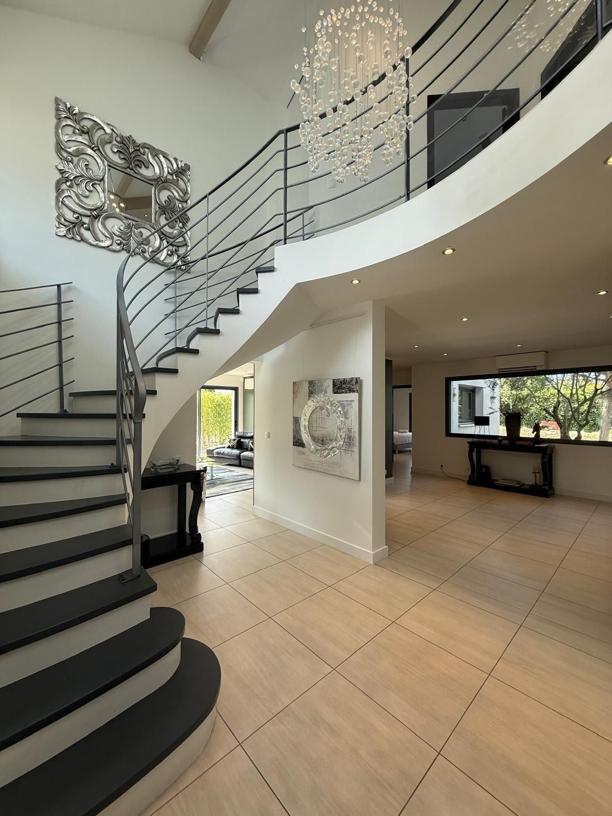 A modern interior with a spiral staircase, a chandelier, and a large window.