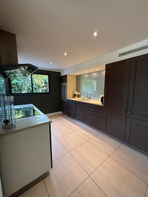 A modern kitchen with dark cabinets, a central island, and a view of greenery outside.