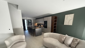 Una sala de estar moderna con un sofá, una mesa de centro de vidrio y una cocina al fondo.