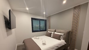 A modern bedroom with a bed, a television mounted on the wall, and a window with blinds. - RIVAGES BAY (Veigy-Foncenex)