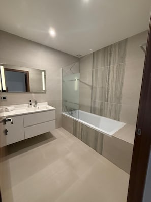 Een moderne badkamer met een douche met glazen wand, een witte wastafel en een grote spiegel.