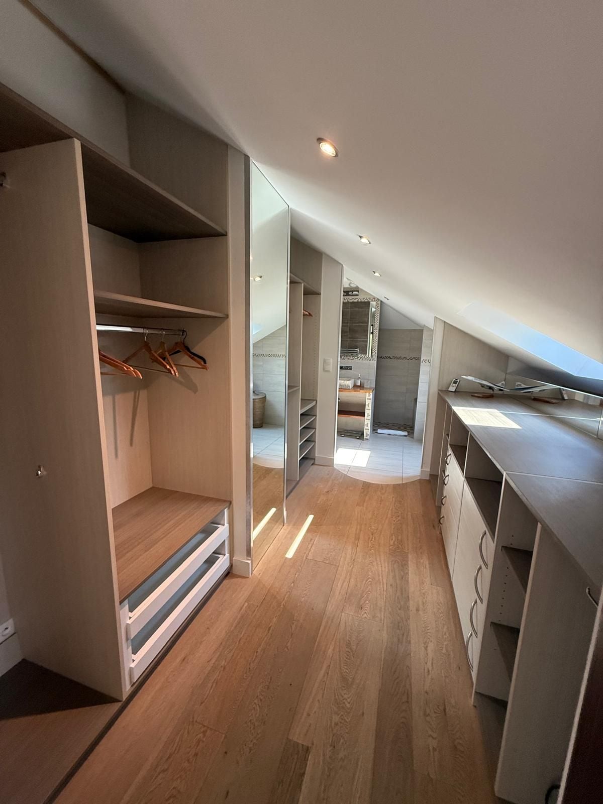 A modern, open-plan space with a wooden floor, built-in shelving, and a kitchen area.