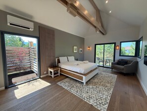 A bedroom with a large bed, a sofa, a sliding glass door leading to an outdoor area, and a ceiling with exposed beams.