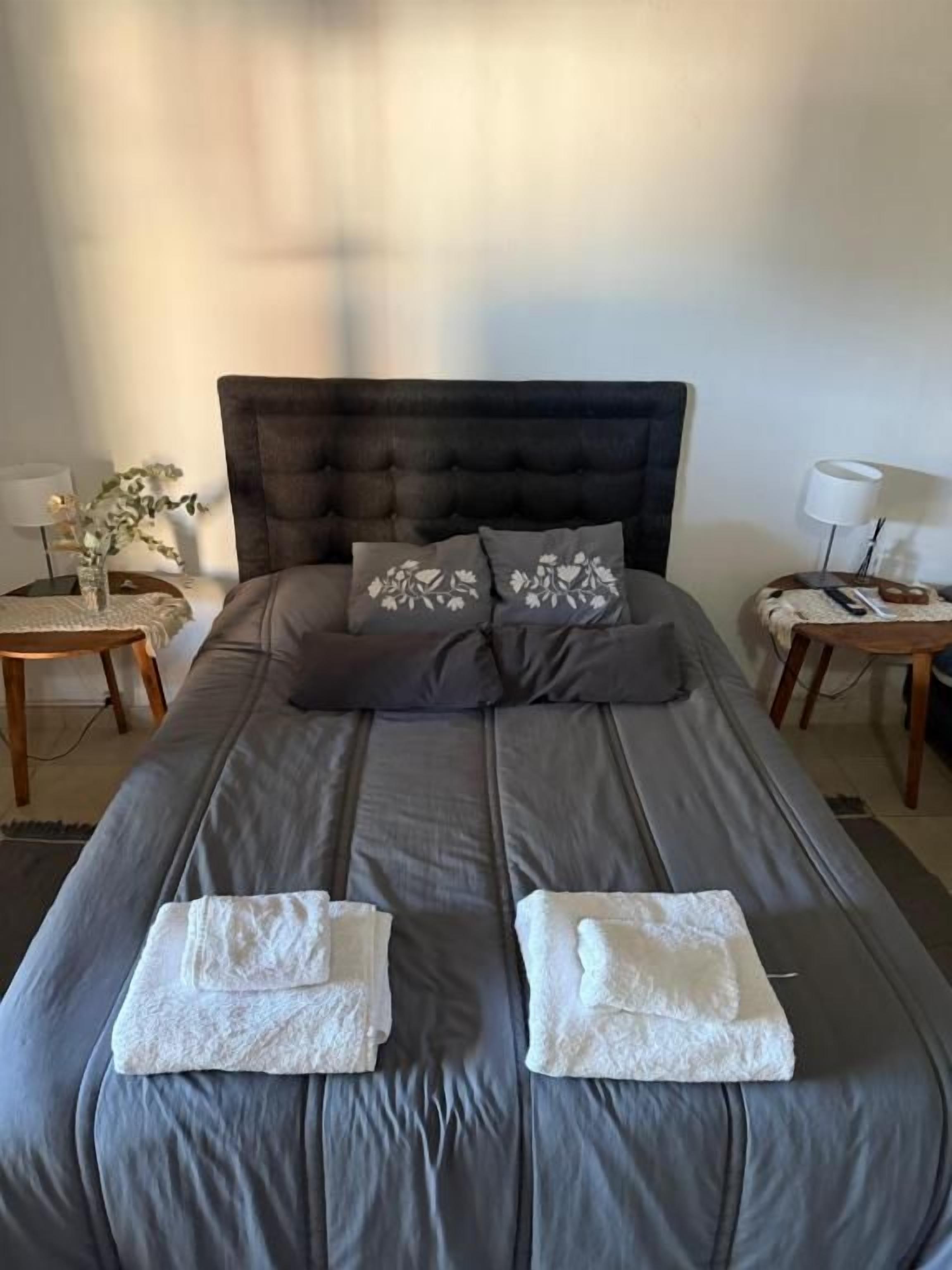 A neatly made bed with a dark headboard, two pillows, and two folded towels.