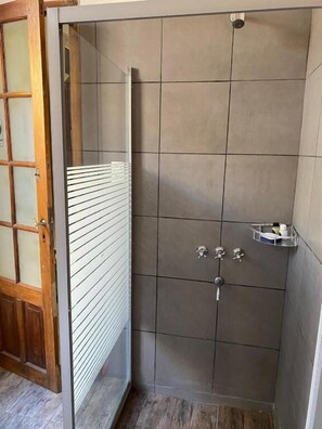 Ducha con pared de azulejos, puerta de madera y un estante pequeño con artículos de aseo.