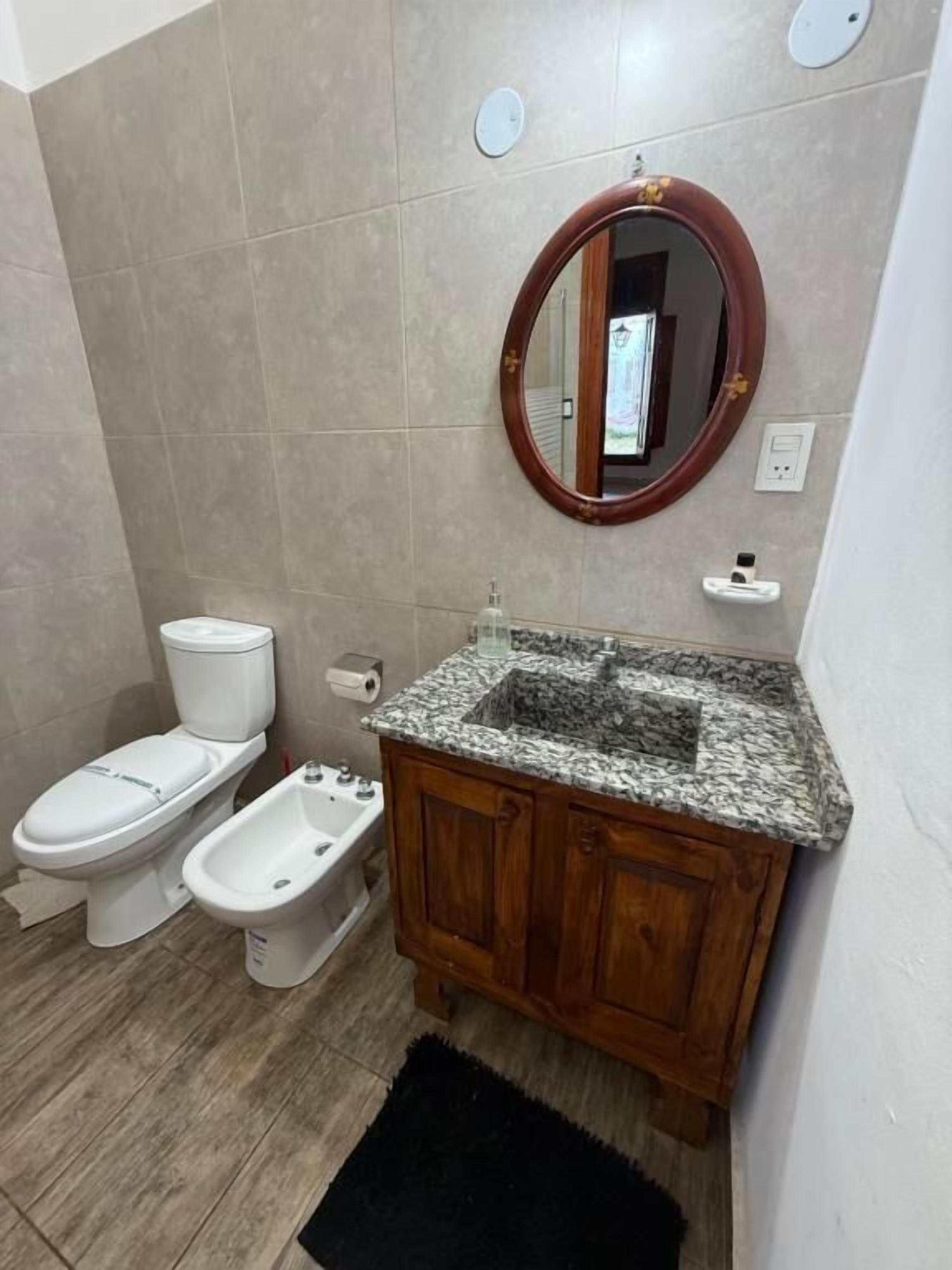 Un baño con inodoro, bidé y tocador con lavamanos y espejo.