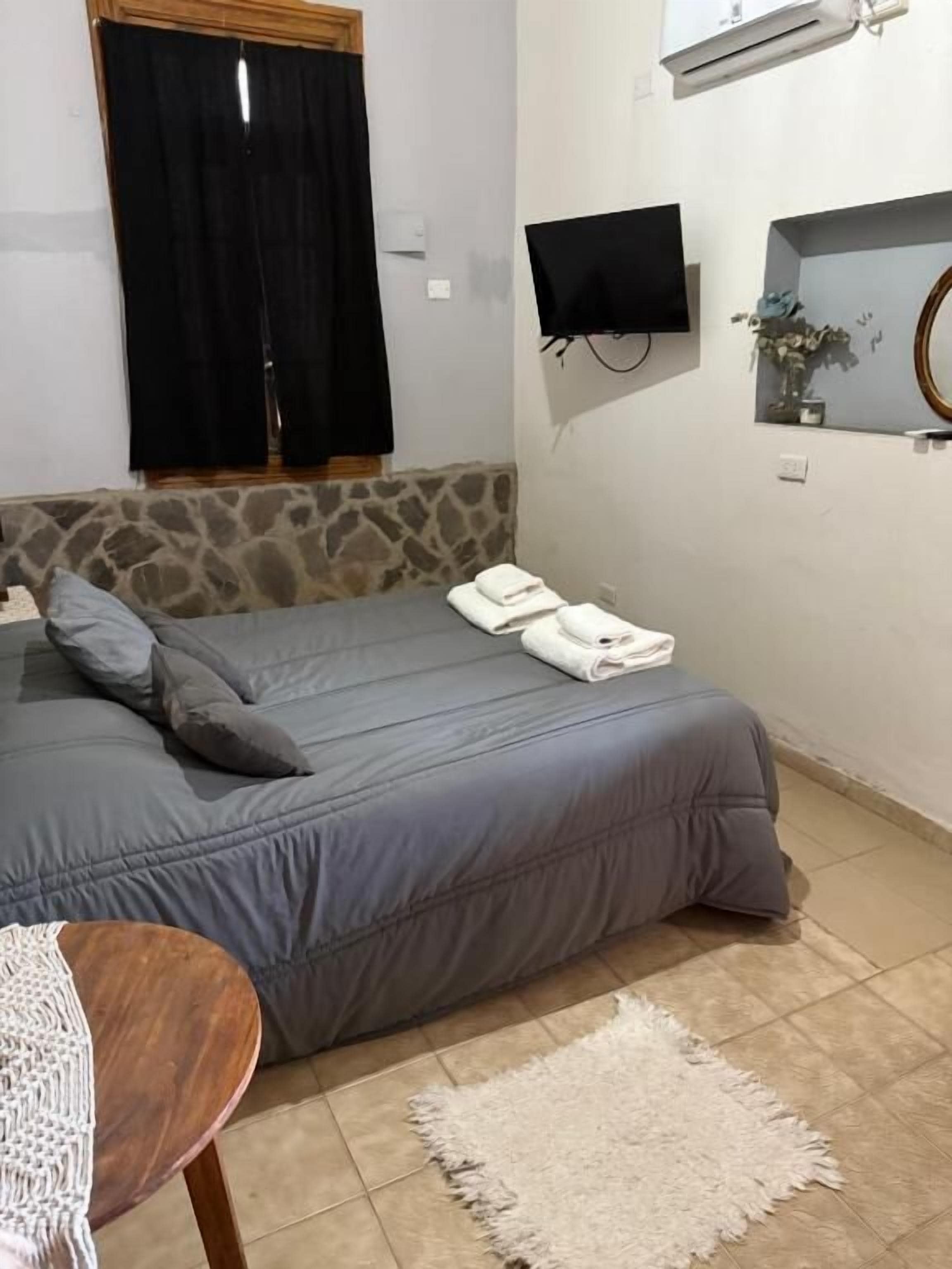 Un dormitorio con cama, televisor de pantalla plana, espejo y ventana con cortinas.