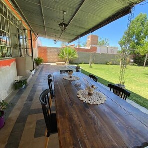 Un área de comedor al aire libre con una mesa de madera larga, sillas negras y centros de mesa decorativos.