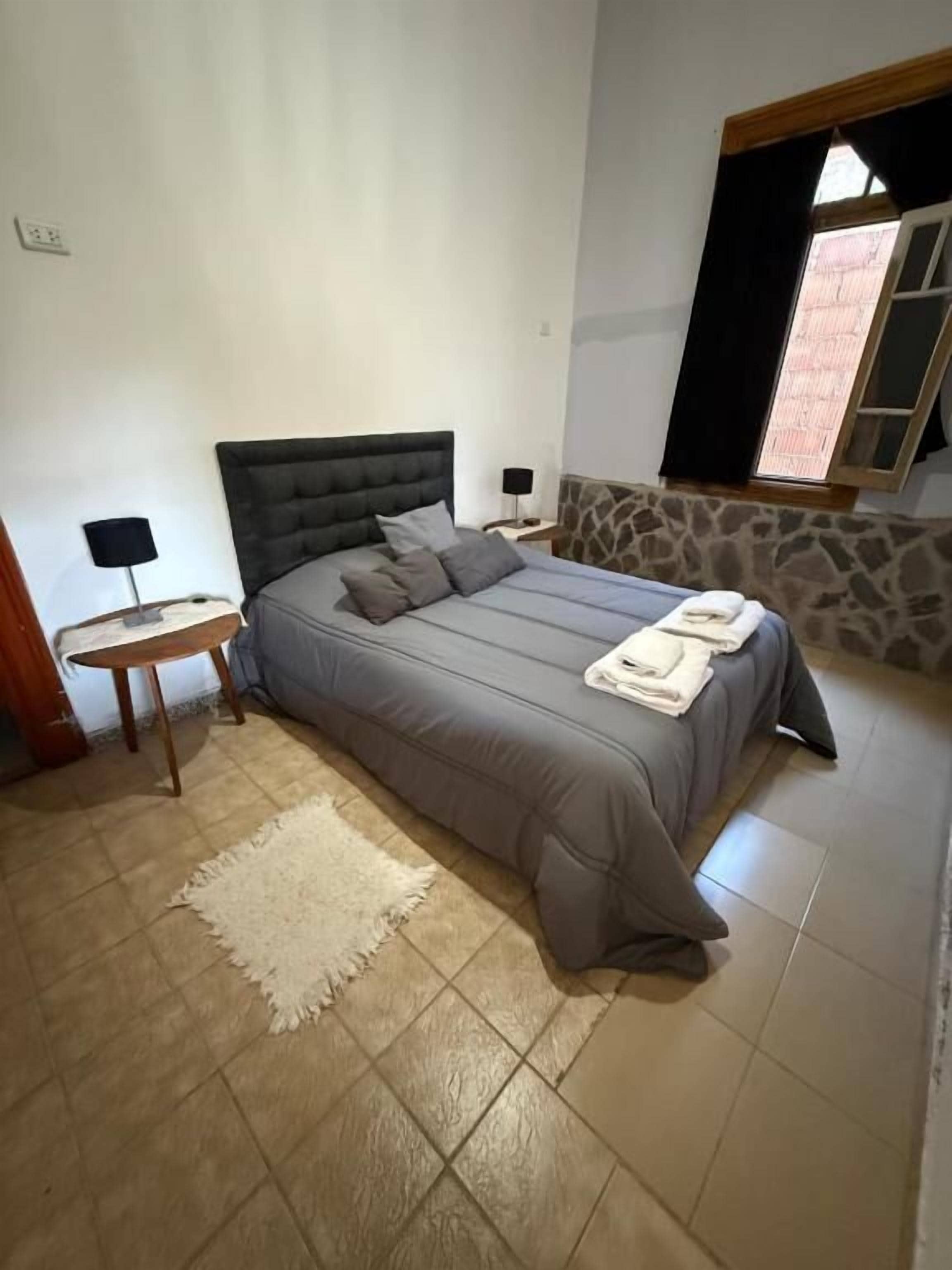 Un dormitorio con una cama grande, una mesita de noche, una lámpara y una ventana con cortinas.