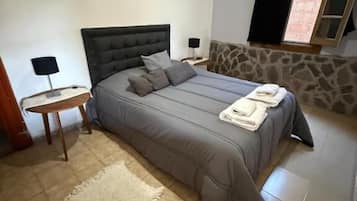 Un dormitorio con una cama grande, una mesita de noche, una lámpara y una ventana con cortinas.