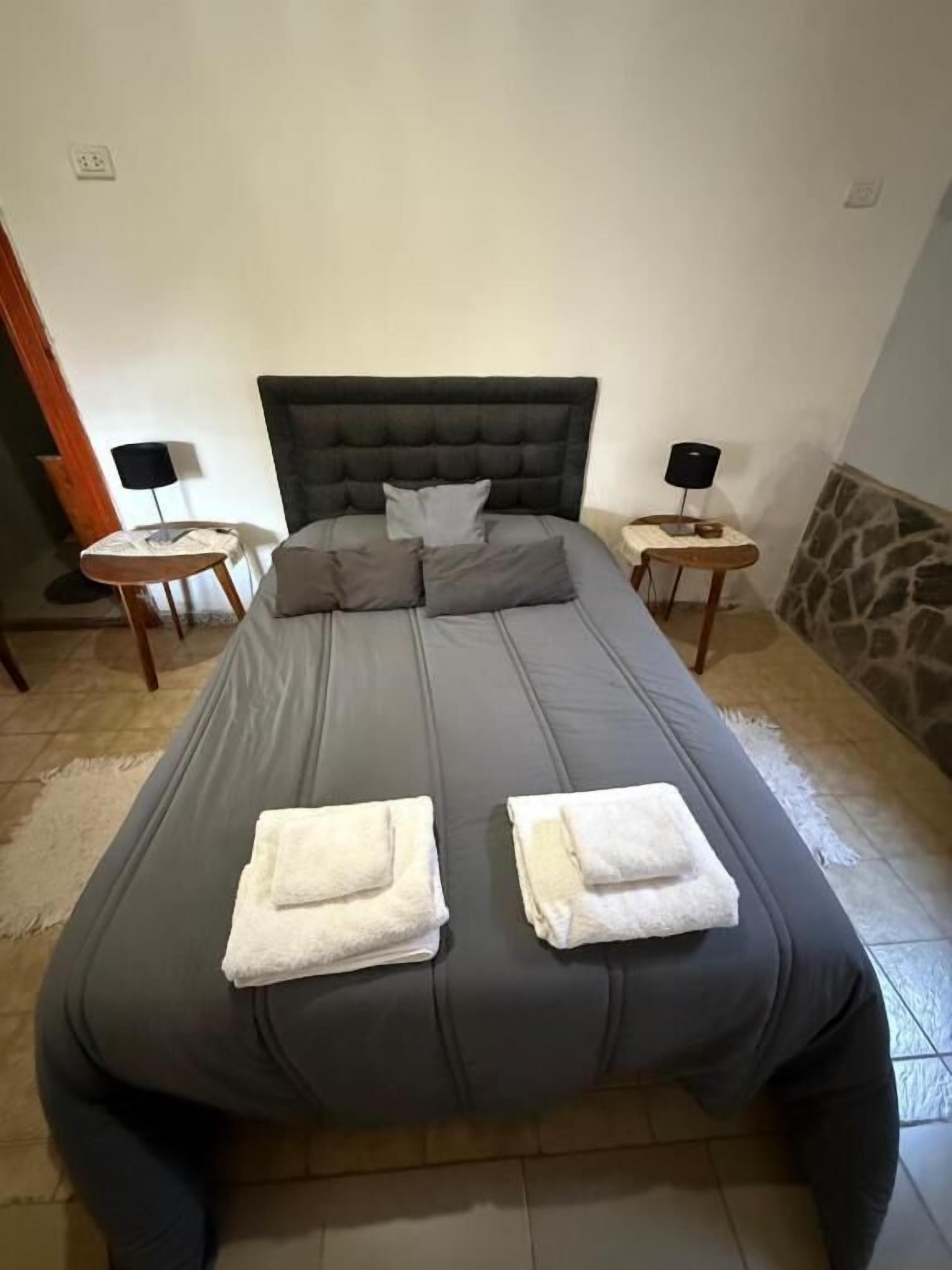 Una cama con cabecera, dos mesitas de noche con lámparas y toallas sobre la cama.