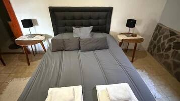 Una cama con cabecera, dos mesitas de noche con lámparas y toallas sobre la cama.