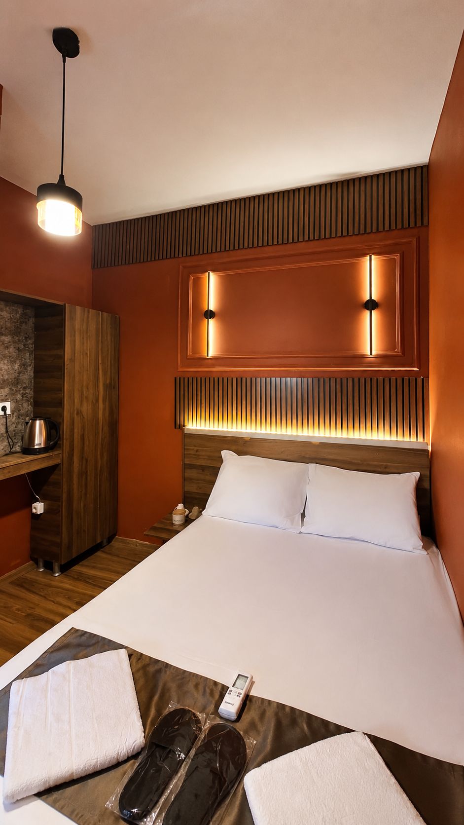 Una camera d'albergo con un letto grande, una testiera in legno, un comodino, un bollitore e un telecomando.