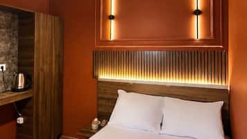 Una camera d'albergo con un letto grande, una testiera in legno, un comodino, un bollitore e un telecomando.