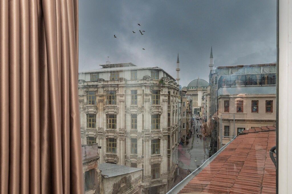 Vista de un paisaje urbano con edificios históricos, incluyendo una mezquita con un minarete, a través de una ventana con cortinas.