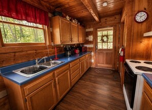 A wooden cabin kitchen with a blue countertop, wooden cabinets, a stove, and a clock on the wall. - Mtn Views + Hot Tub | 10 Min to Pigeon Forge (Sevierville)