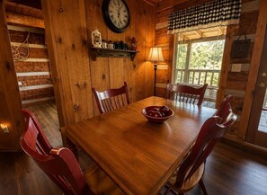 A wooden dining room with a round table, red chairs, a clock, and a window with a view of greenery. - Mtn Views + Hot Tub | 10 Min to Pigeon Forge (Sevierville)