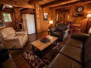 A cozy cabin interior with a wooden interior, leather furniture, a dining area, and a kitchen with a refrigerator. - Mtn Views + Hot Tub | 10 Min to Pigeon Forge (Sevierville)