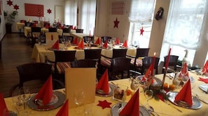 Restaurante com mesas preparadas para refeições, com guardanapos vermelhos e velas.