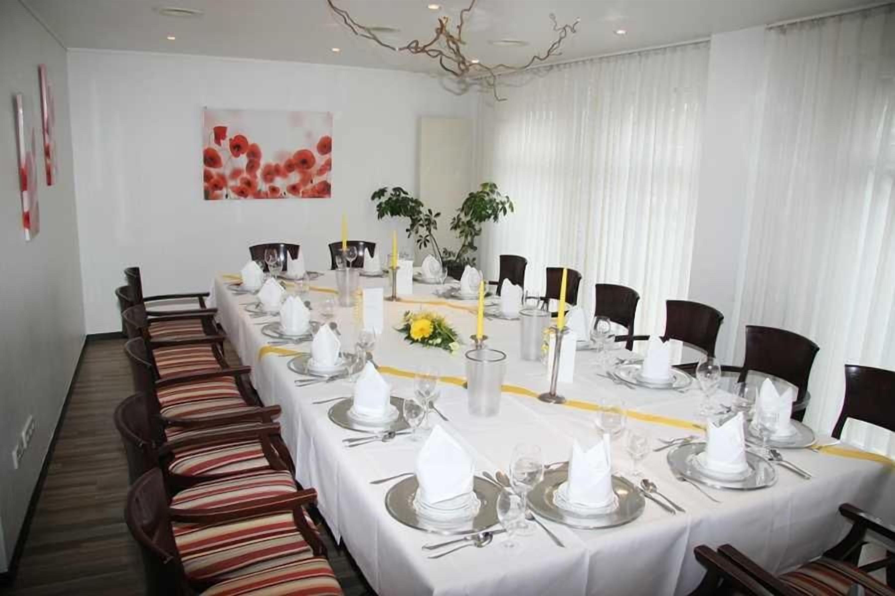 Una larga mesa de comedor dispuesta para un evento formal, con manteles blancos, cubiertos y velas.