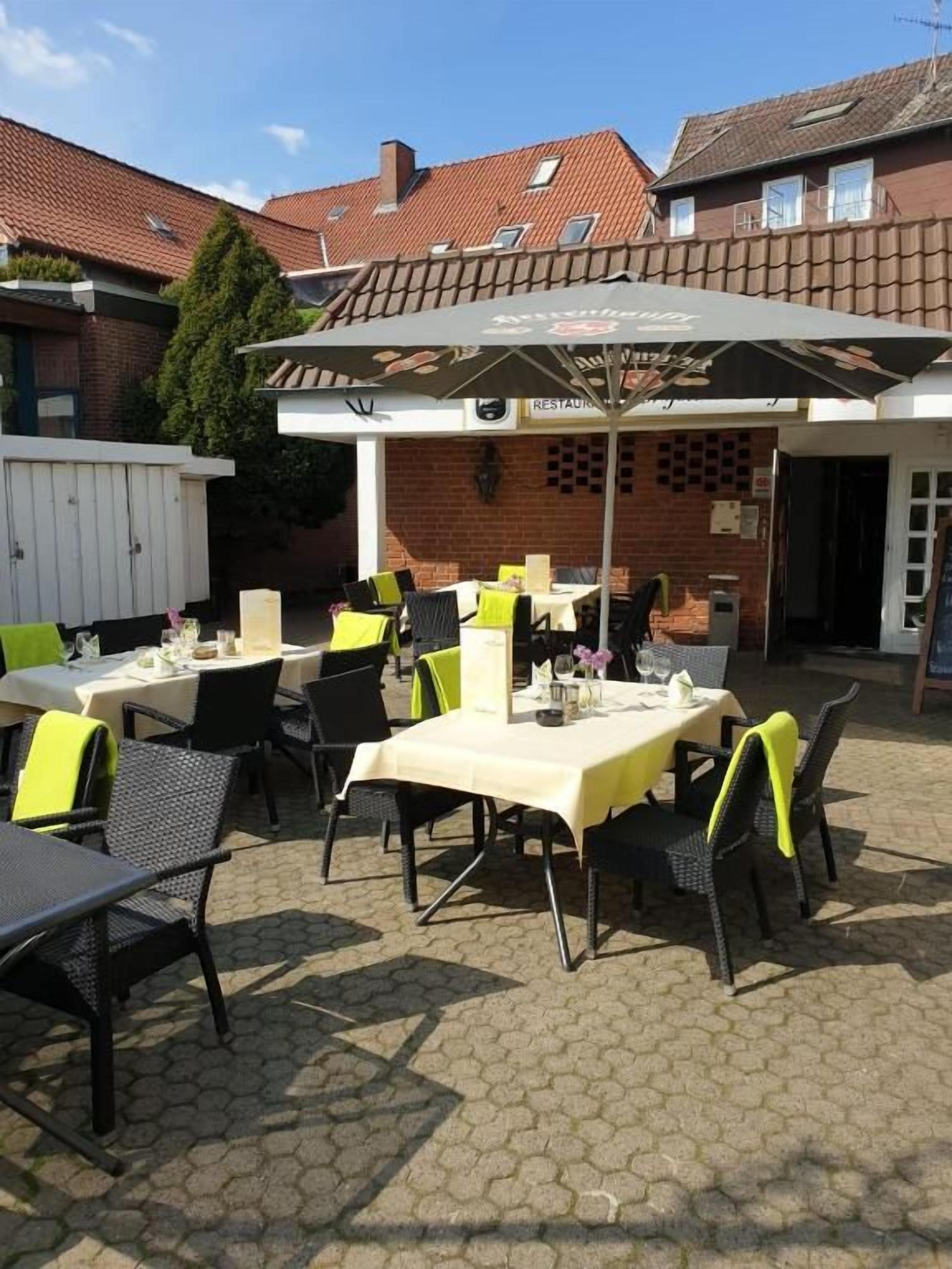 An outdoor patio with tables and chairs, a covered seating area, and a brick building in the background.