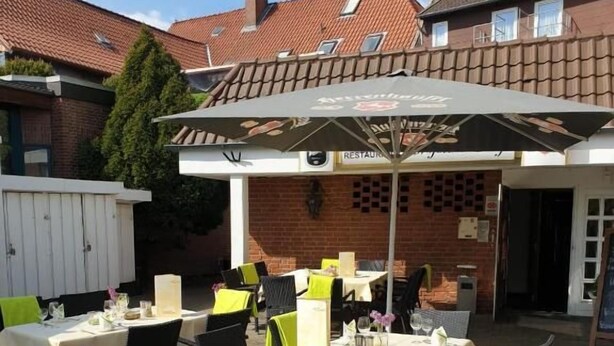 Un patio esterno con tavoli e sedie, un'area salotto coperta e un edificio in mattoni sullo sfondo.