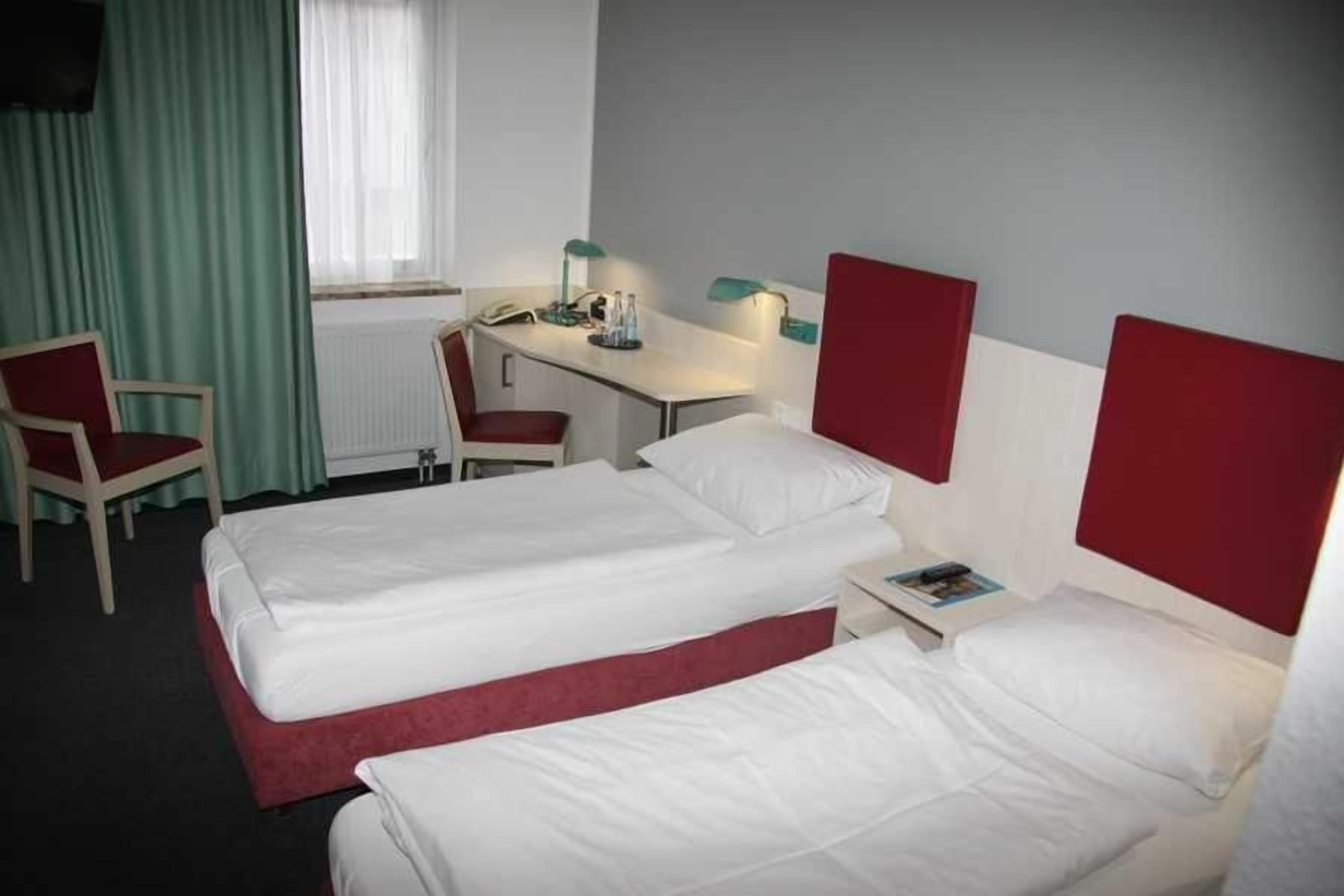 A hotel room with two beds, a desk, a chair, and a window with curtains.