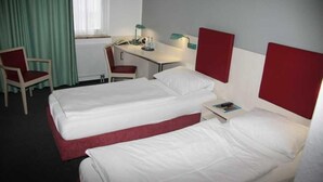 Una camera d'albergo con due letti, una scrivania, una sedia e una finestra con tende.