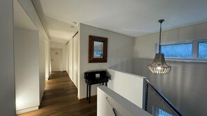 A modern interior with a wooden floor, a black desk, a hanging light fixture, and a view through a window.