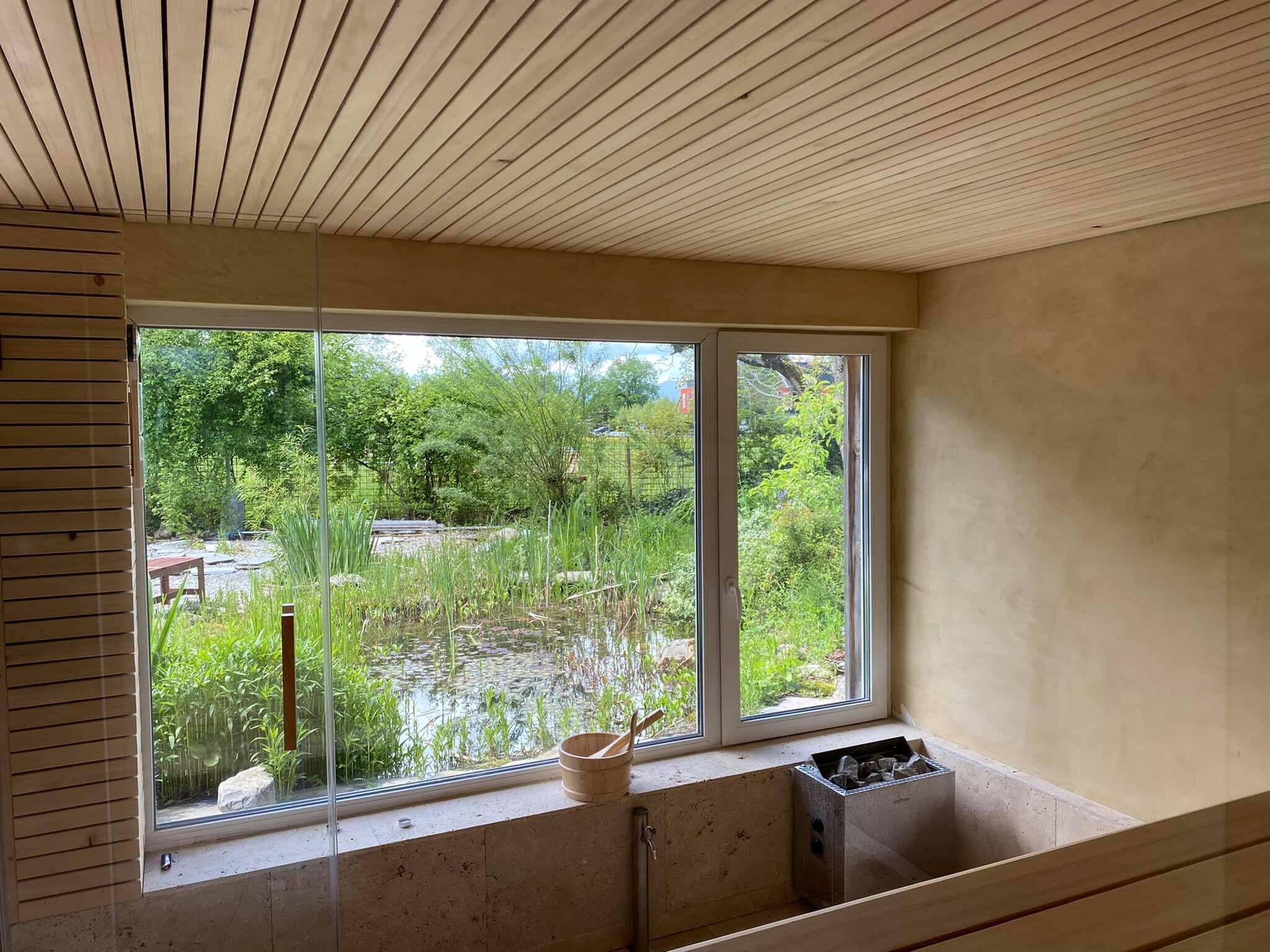 A room with a large window overlooking a pond and greenery.