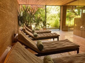 Un espace spa doté de plusieurs tables de massage, d’un plafond en bois et offrant une vue sur la verdure grâce à de grandes portes vitrées.