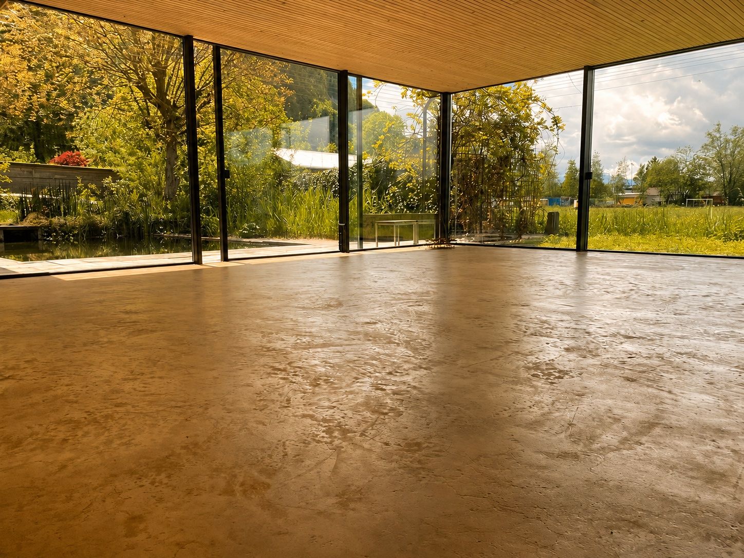 A spacious room with large glass windows, a concrete floor, and a wooden ceiling.