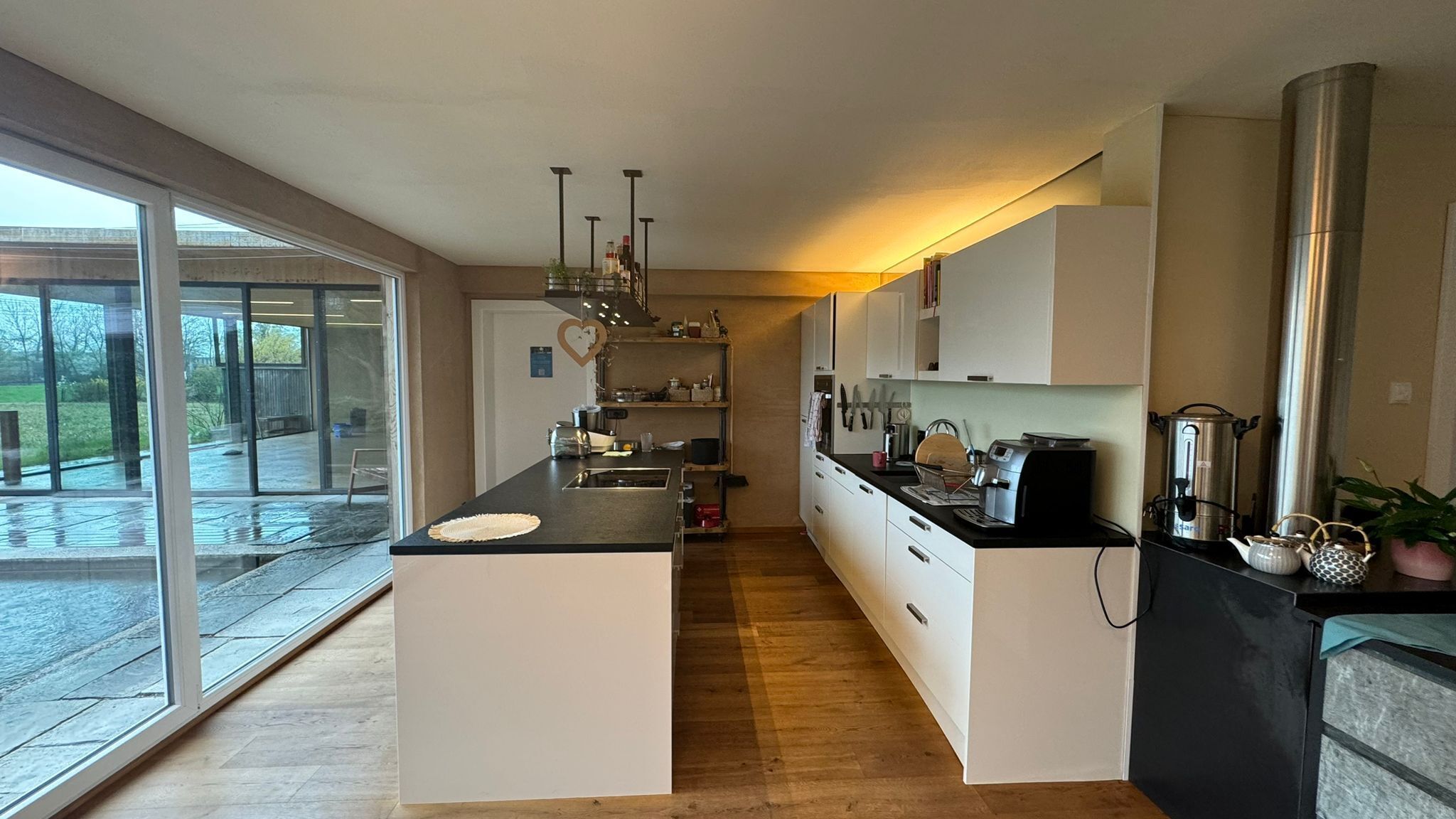 A modern kitchen with a central island, white cabinetry, and a large sliding glass door leading to an outdoor area.