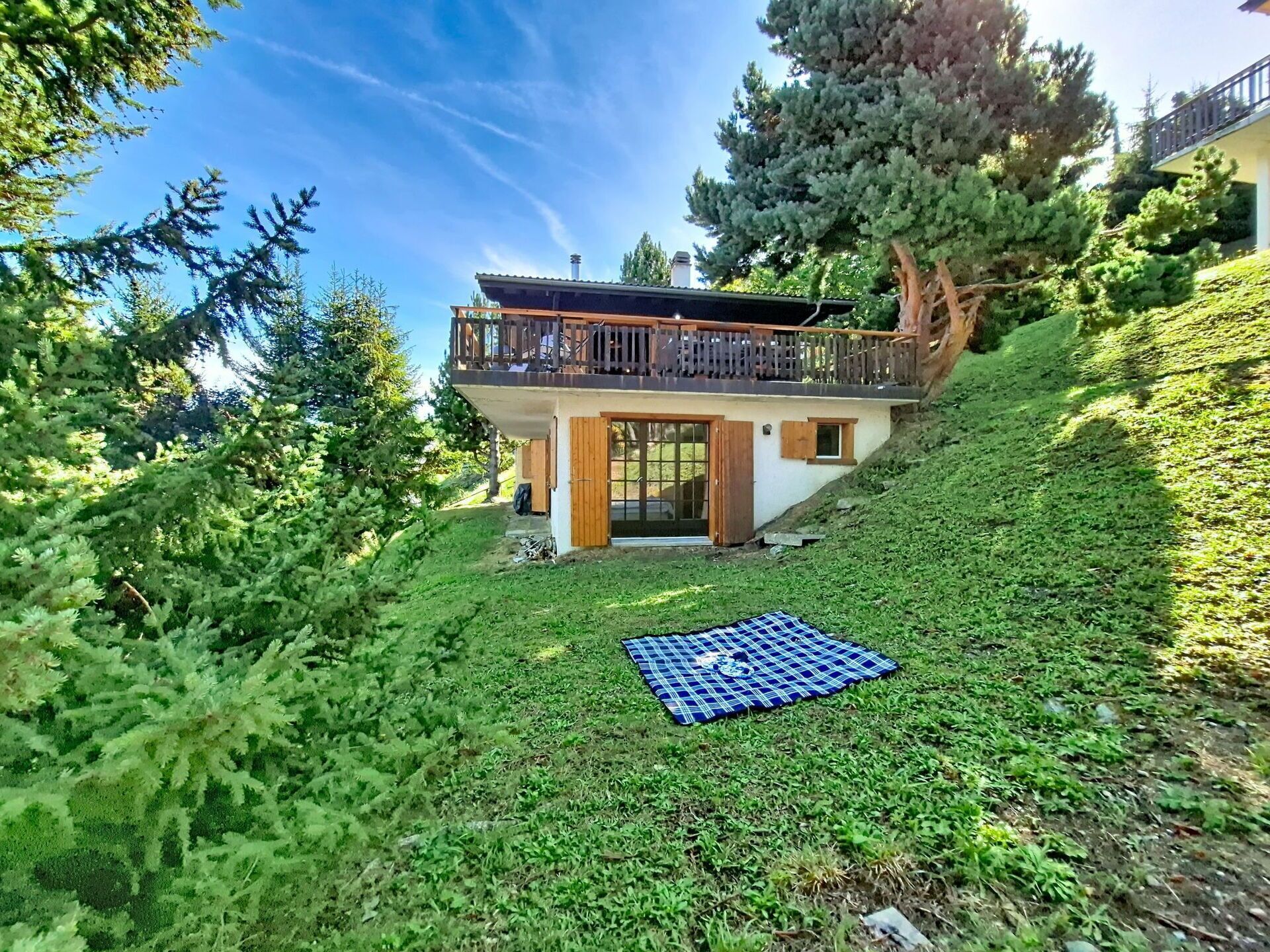 A two-story house with a balcony, surrounded by lush greenery and trees.
