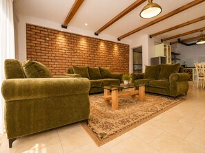 A living room with a brick wall, green sofas, a glass coffee table, and a patterned rug. - Mwalosun Luxury Vintage Apartments (Kampala)
