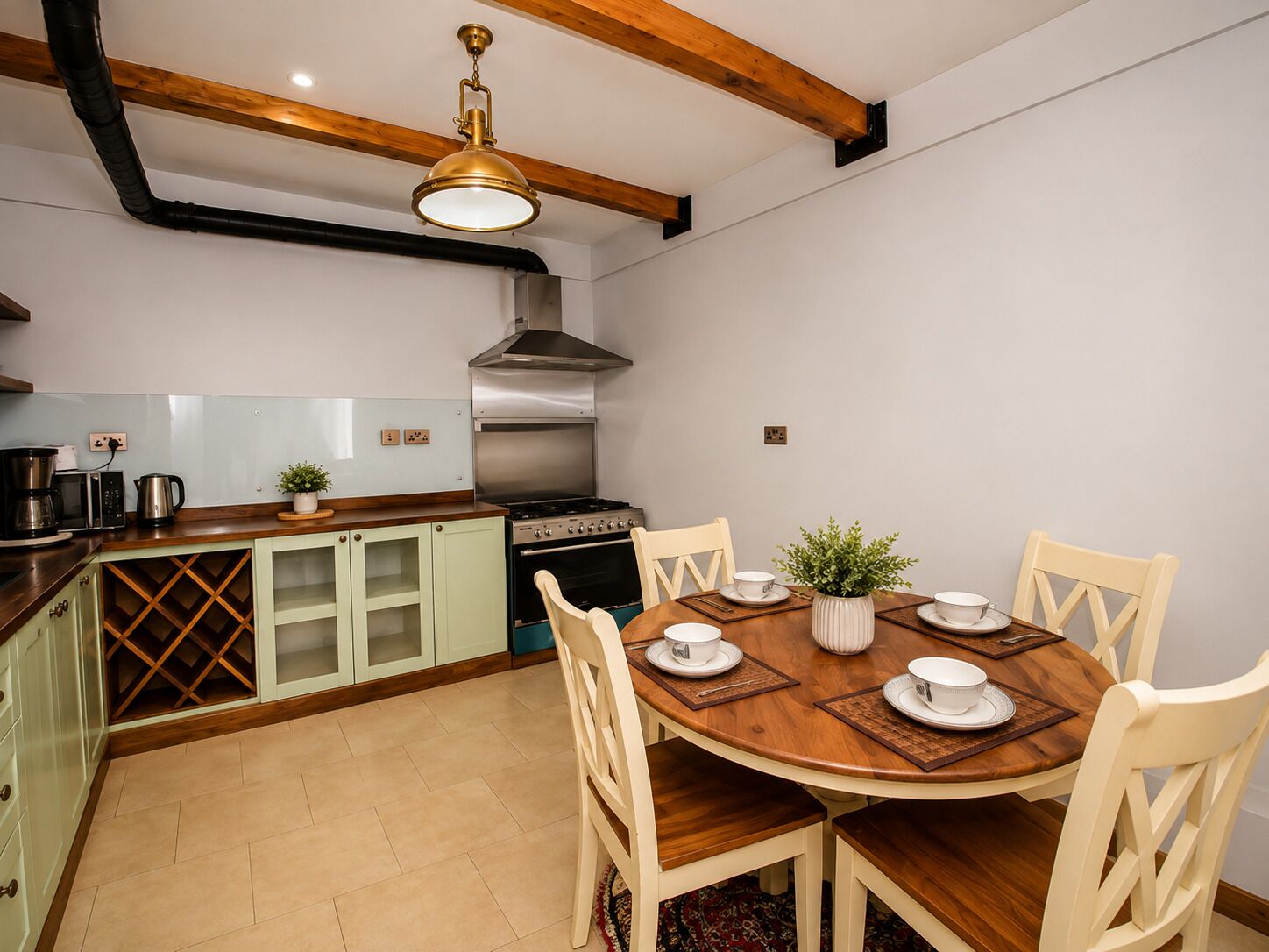 A kitchen with a round wooden table, white chairs, a stove, and a hanging light fixture.