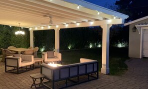 Un patio exterior con pérgola, mobiliario y una chimenea.