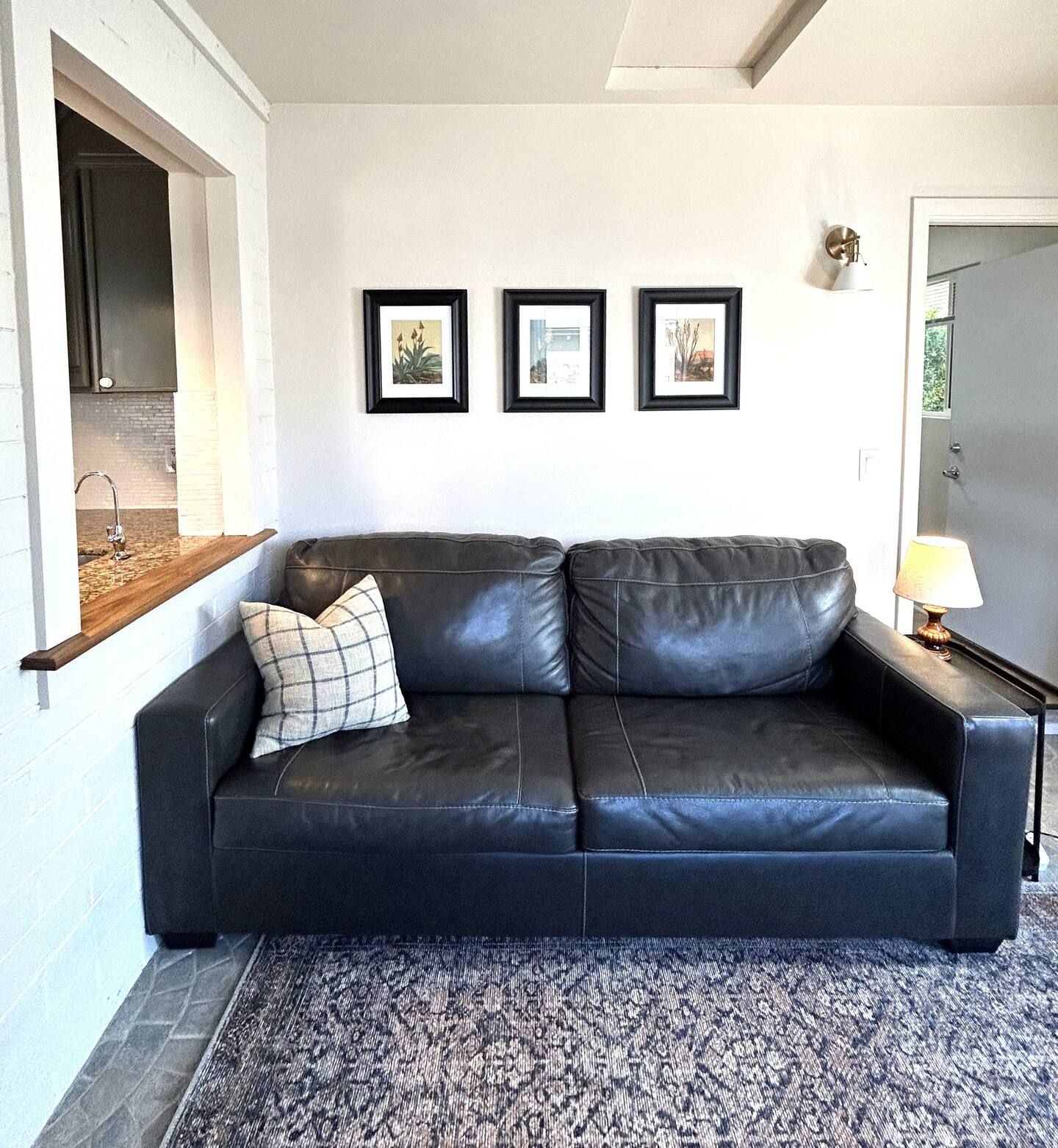 Un canapé en cuir noir agrémenté d’un coussin à carreaux, d’un tapis à motifs et de trois tableaux encadrés accrochés au mur.