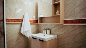 A bathroom with a marble wall, a wooden vanity, a sink, a towel, and a mirror.